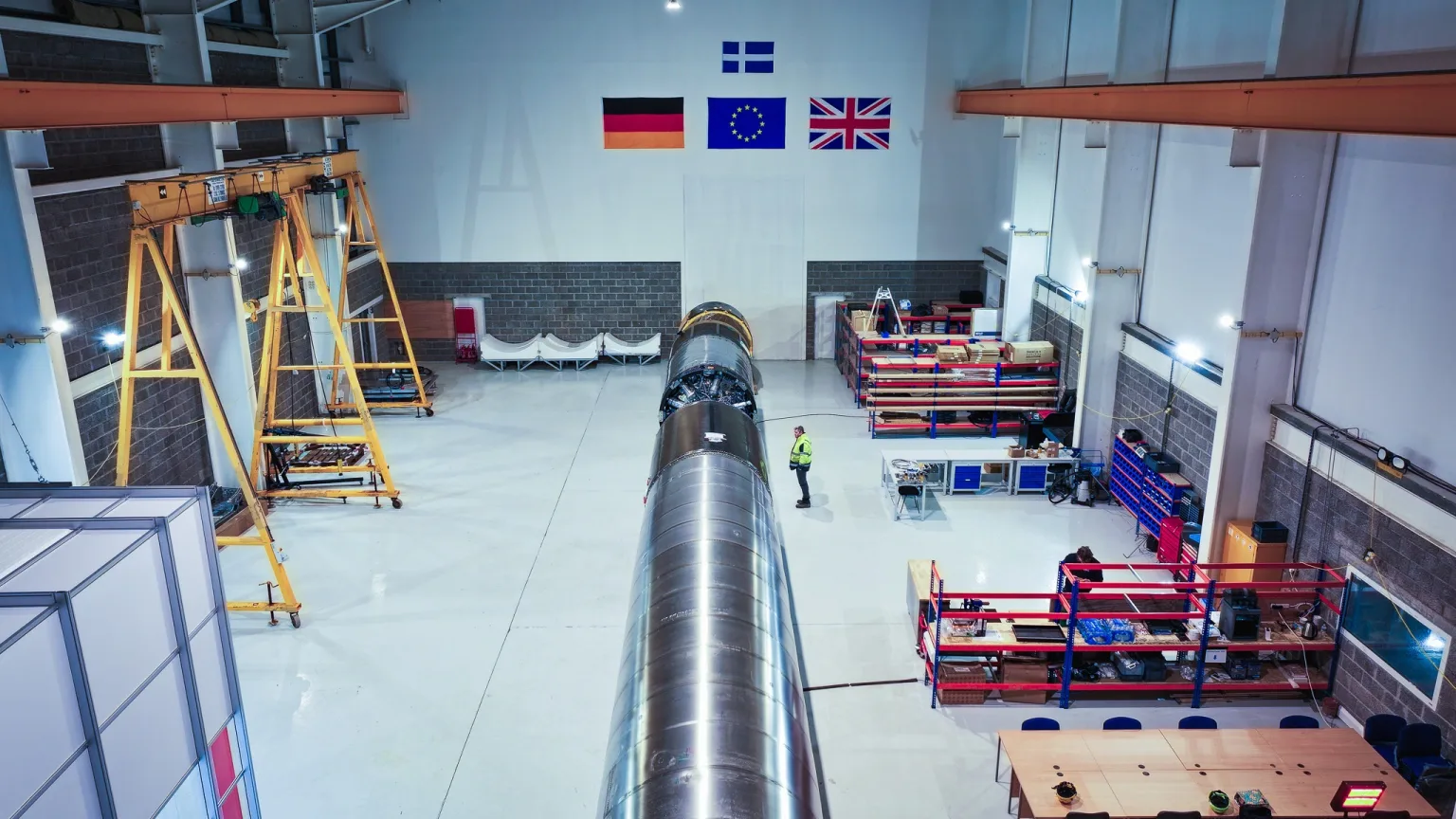 The fully integrated RFA One rocket lying horizontal in the assembly hangar at SaxaVord, a technician beside it for scale.