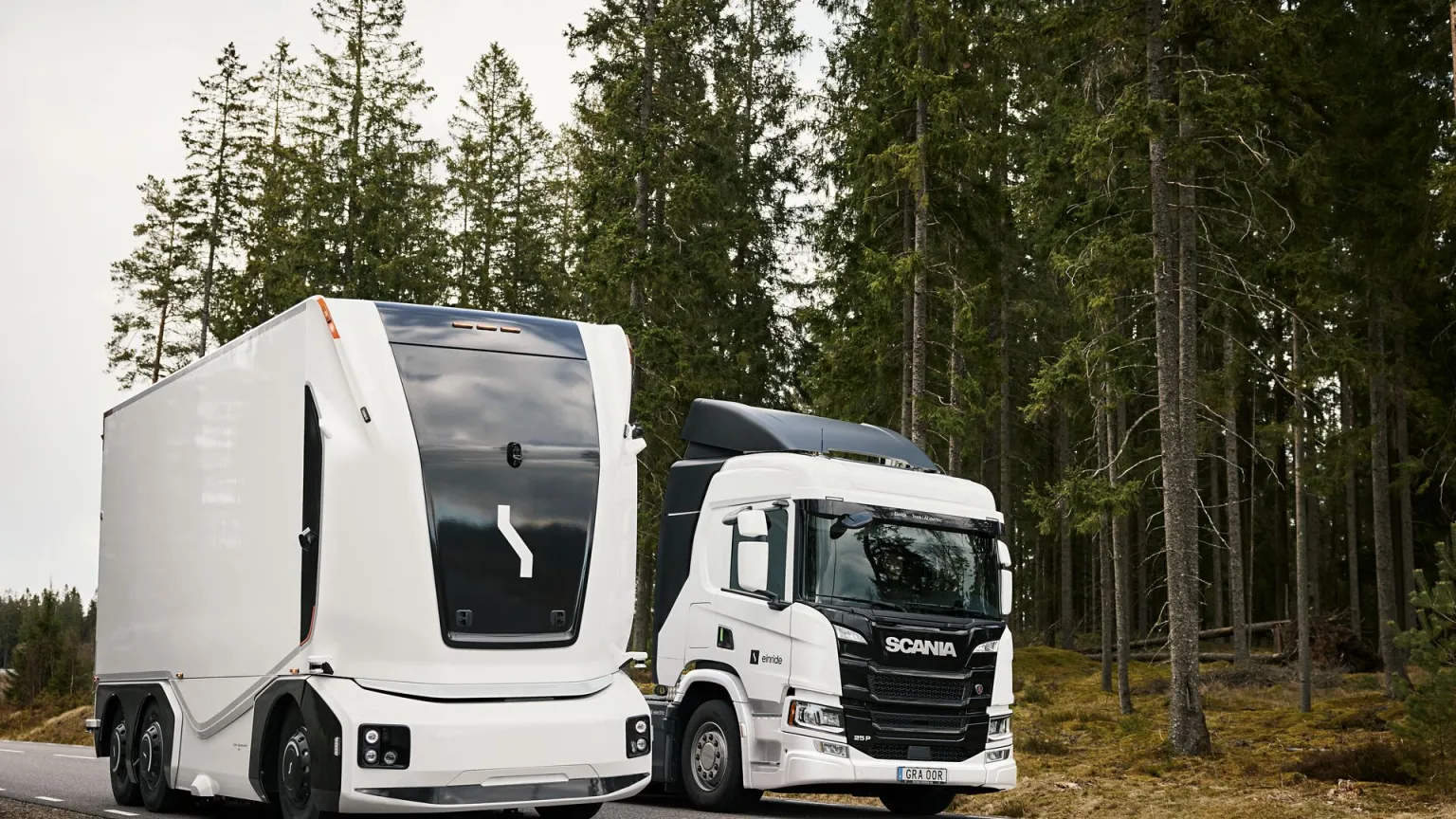 An Einride autonomous truck and a driver-operated Einride electric Scania truck side by side on a forest road.
