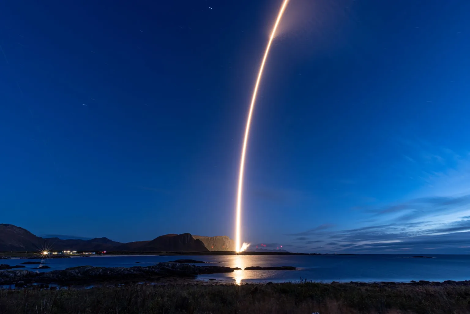 Spectrum rising from Andøya Spaceport at night, leaving a bright arc across the deep-blue sky above the Norwegian coast.