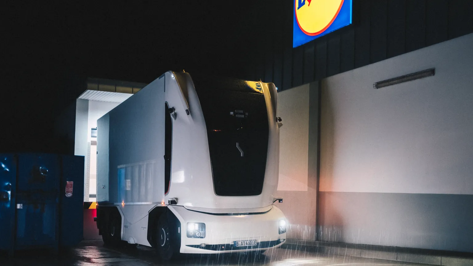 Einride's cab-less autonomous truck leaving a Lidl loading area at night in the rain.