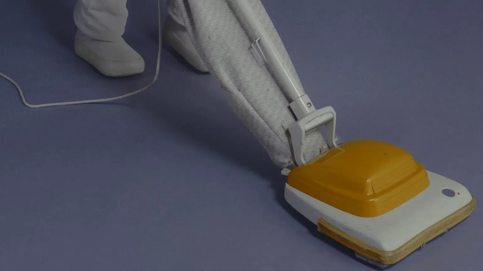 A NEO robot pushing an upright vacuum cleaner across a floor.
