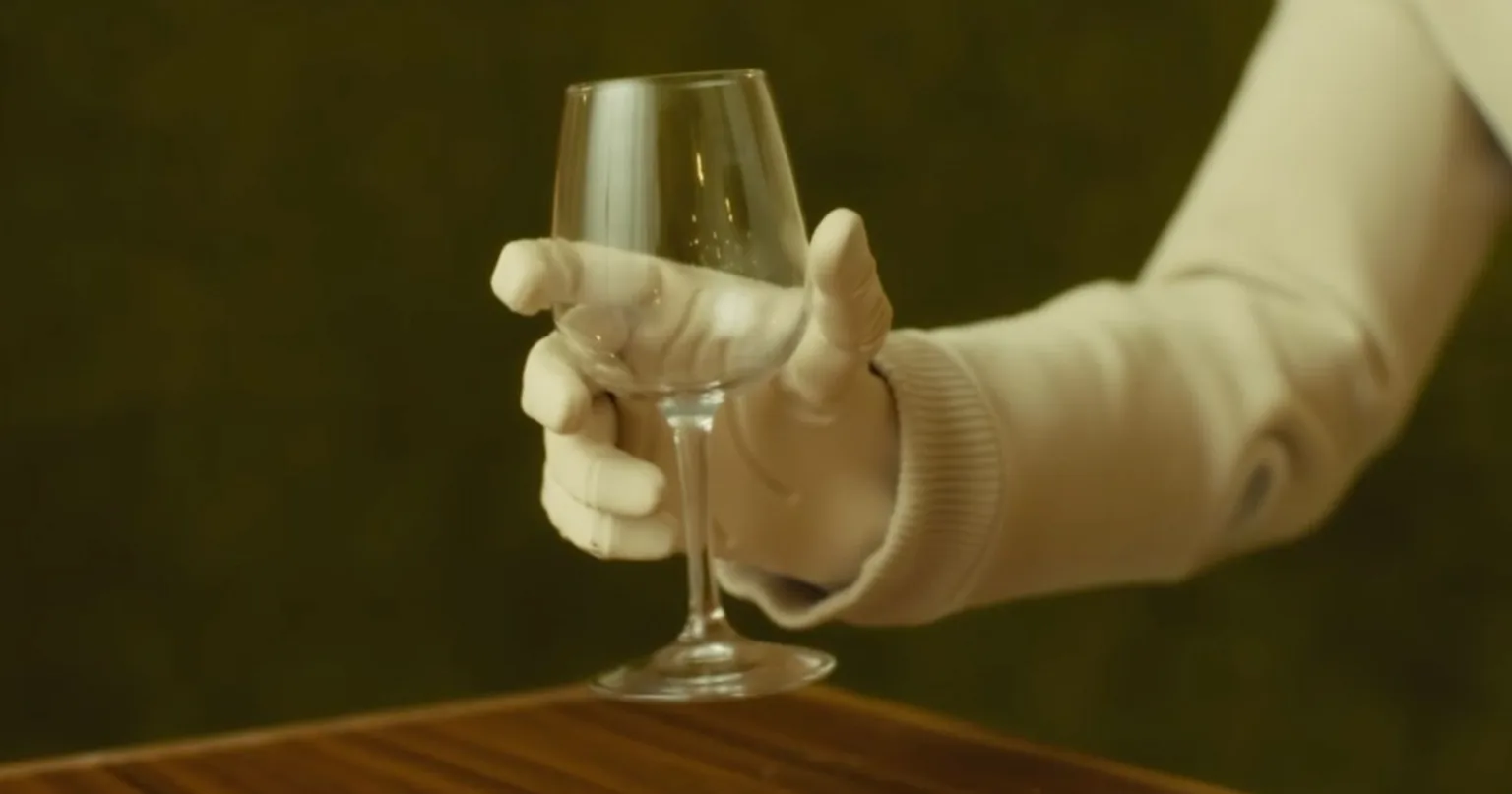 NEO's fabric-covered robotic hand holding a delicate wine glass by its bowl.