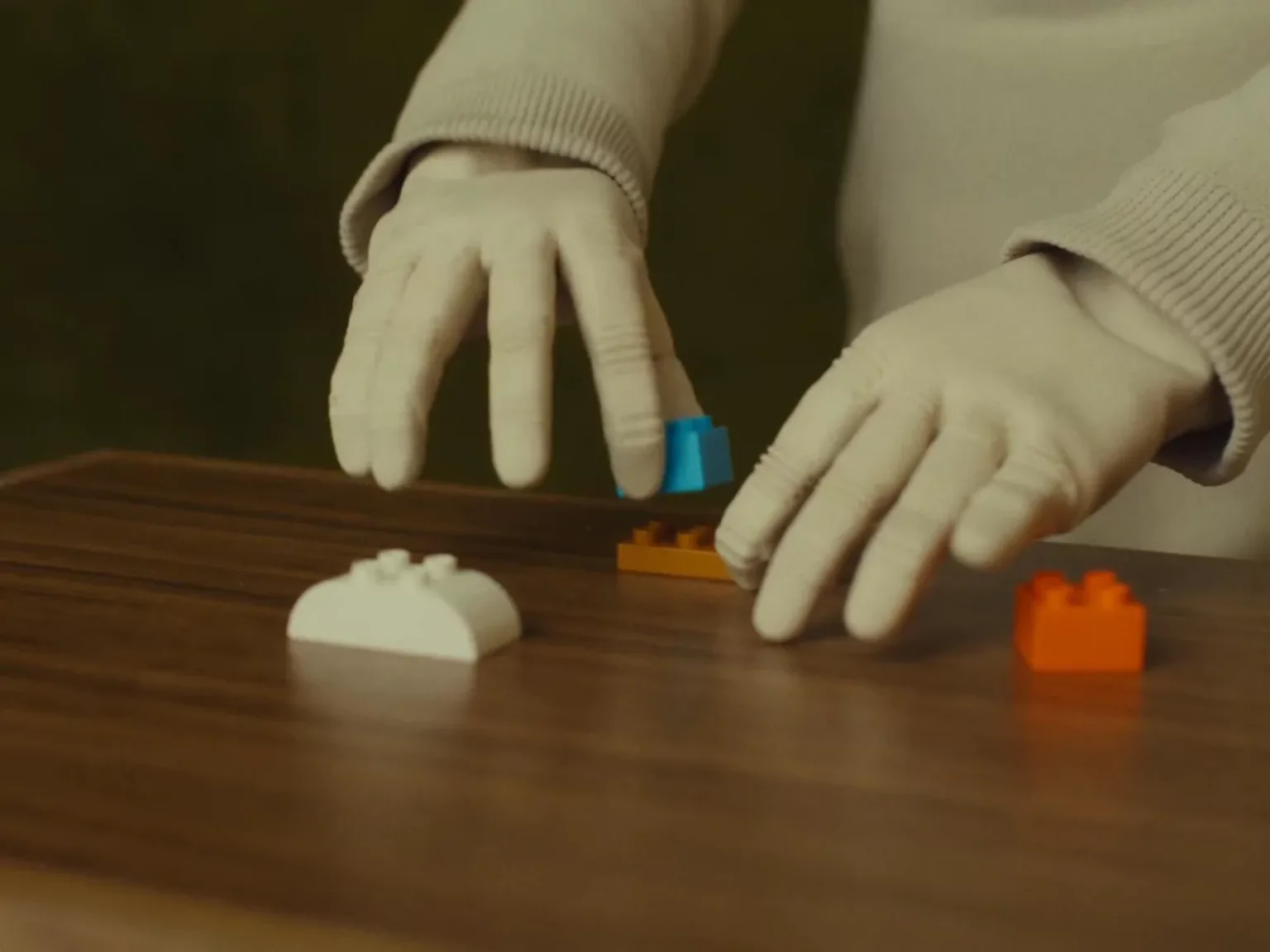 Both of NEO's fabric-covered hands manipulating small colorful construction blocks on a table.
