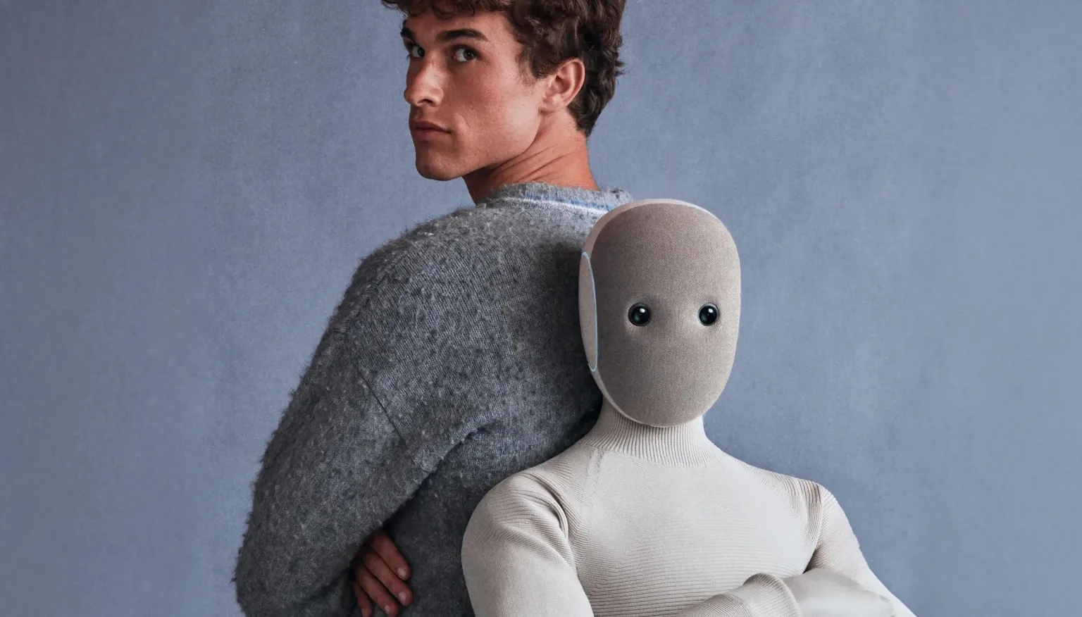 A NEO humanoid robot in a cream knit bodysuit standing back-to-back with a young man.