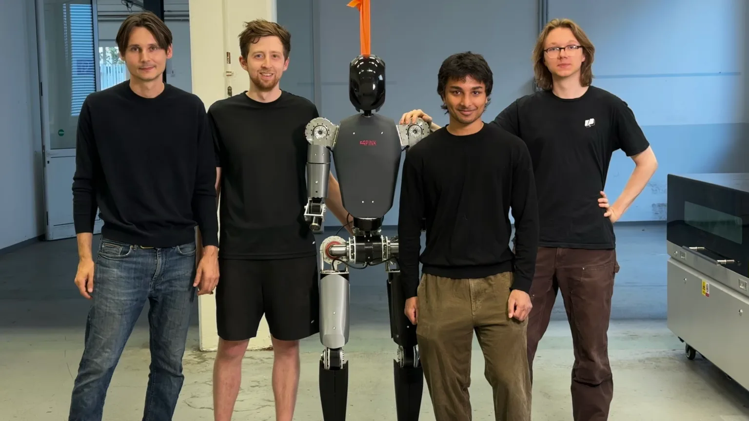 Four Pink Robotics team members standing with the P0 humanoid robot in their workshop.