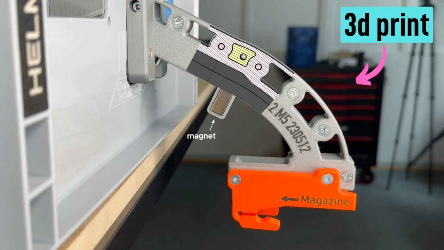 A close-up of a grey 3D-printed screw dispenser with an orange removable magazine and a labelled magnet.