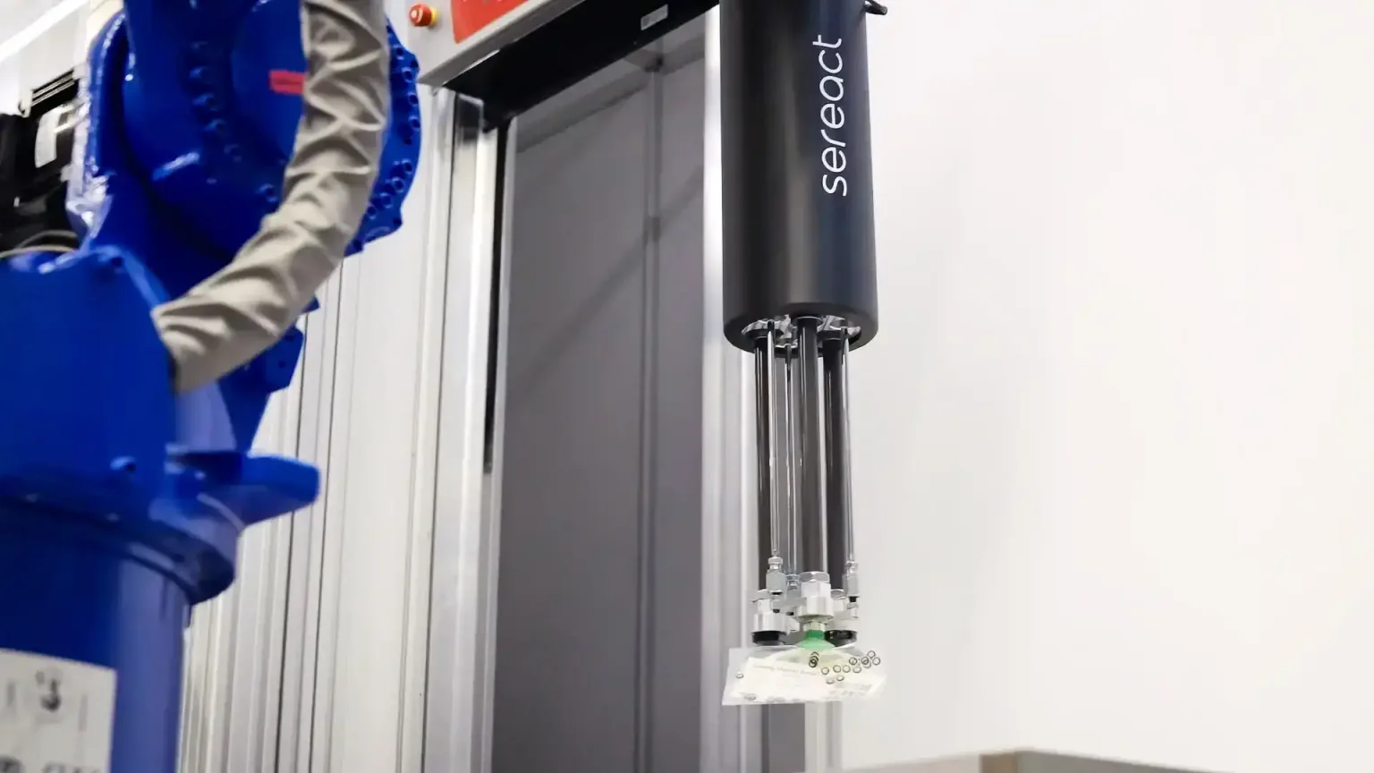 A Sereact-branded gripper on an industrial robot arm picking a packaged item in a facility.