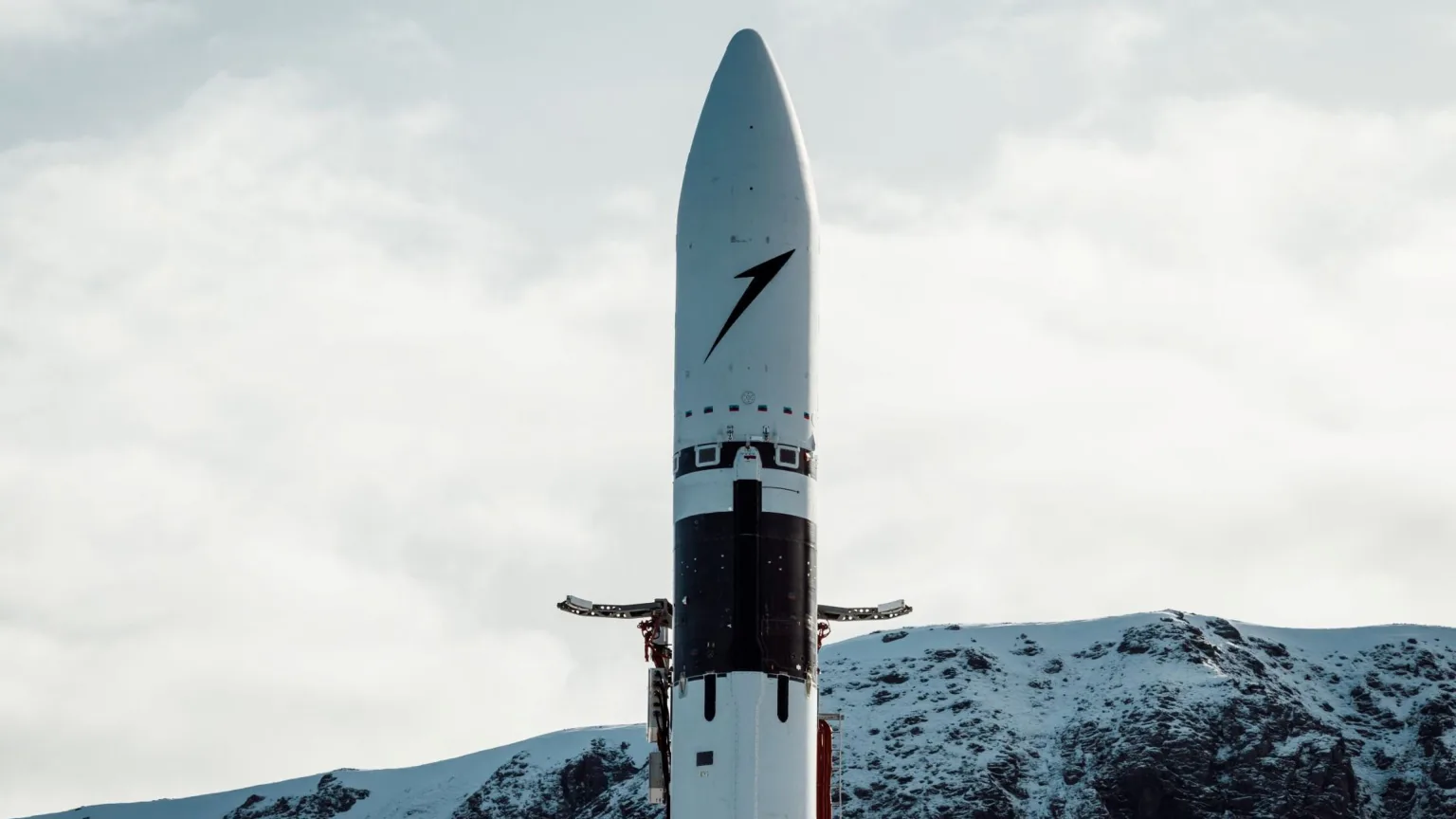 The fairing section of Isar Aerospace's Spectrum rocket standing in front of snowy mountains.