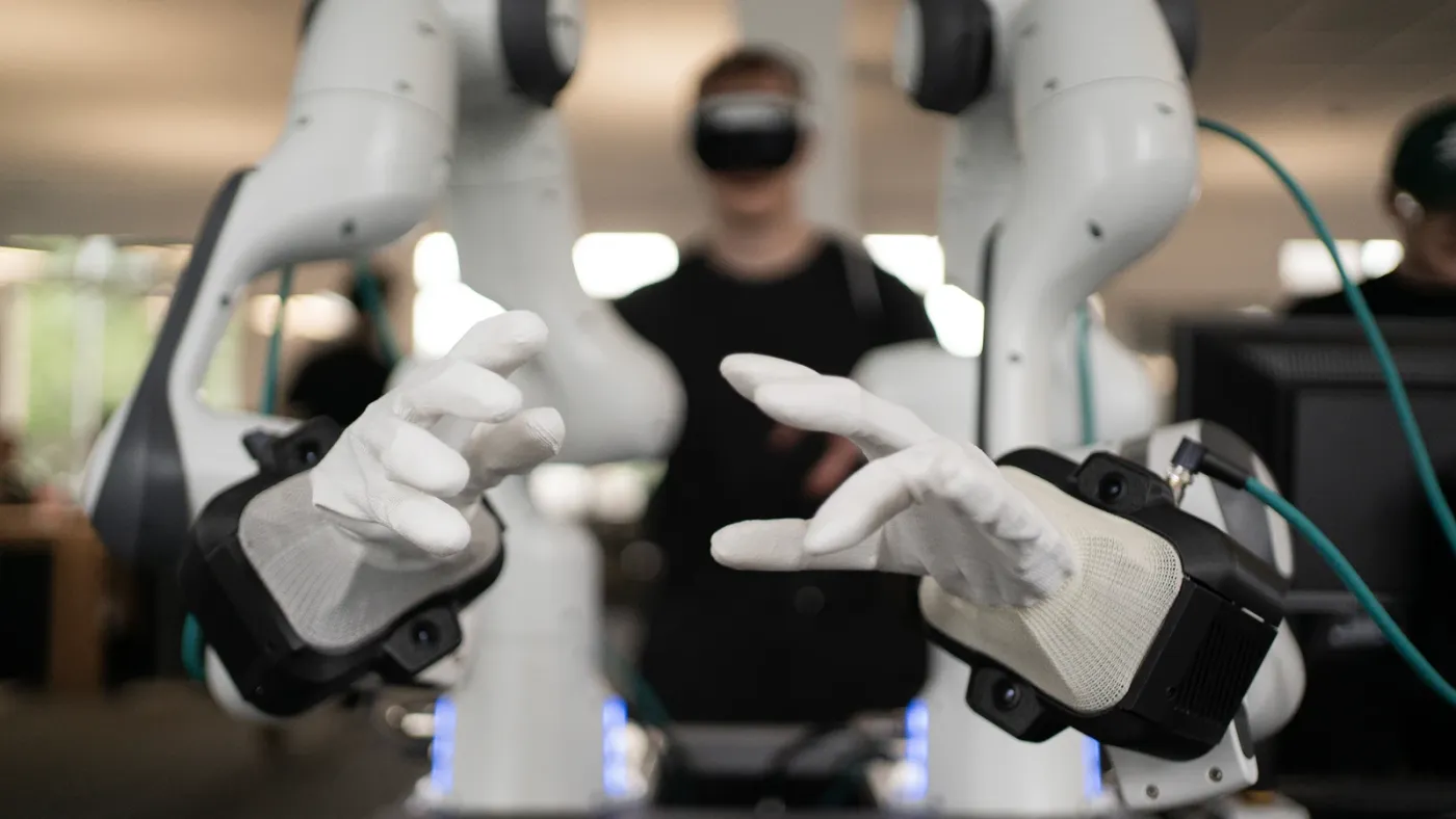 An operator in a VR headset teleoperating two robot arms fitted with mimic's dexterous hands.